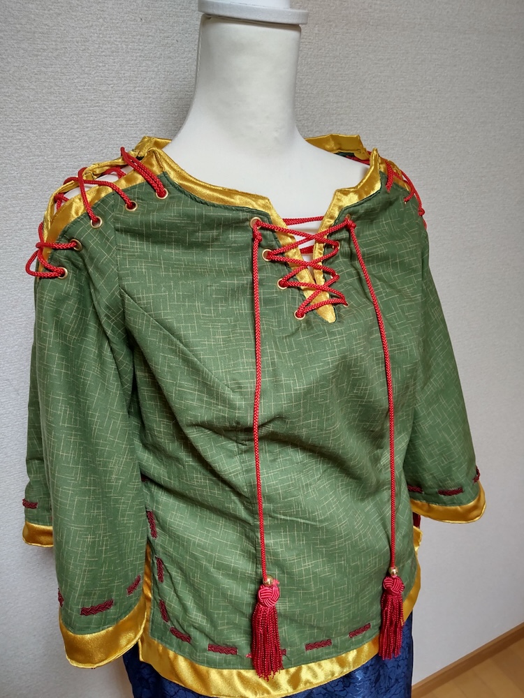 製作した日白残無の赤いタッセルがぶら下がった緑と金の布生地の上着