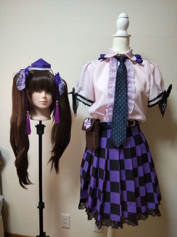 ツインテールにリボンと頭襟の髪飾りがついたウィッグと黒と紫の市松模様のプリーツスカートと胸と衿にフリルがついたブラウス