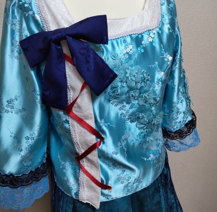 ジャケットの胸元についた青いリボンと襟に編み込まれた赤いリボン