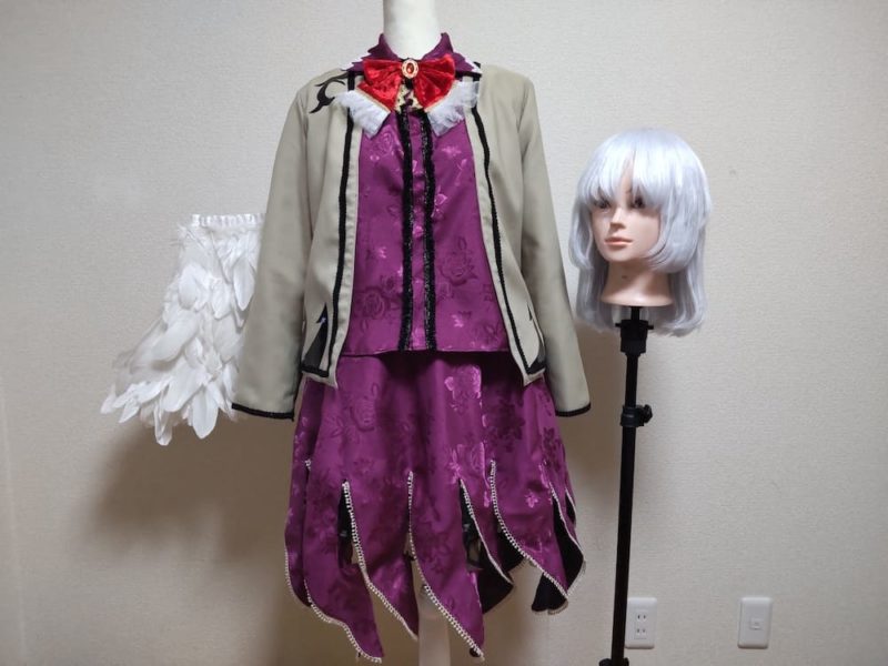 紫色のブラウスと暗い肌色のジャケット、ボブヘアのウィッグとジャケットから生えた白い翼